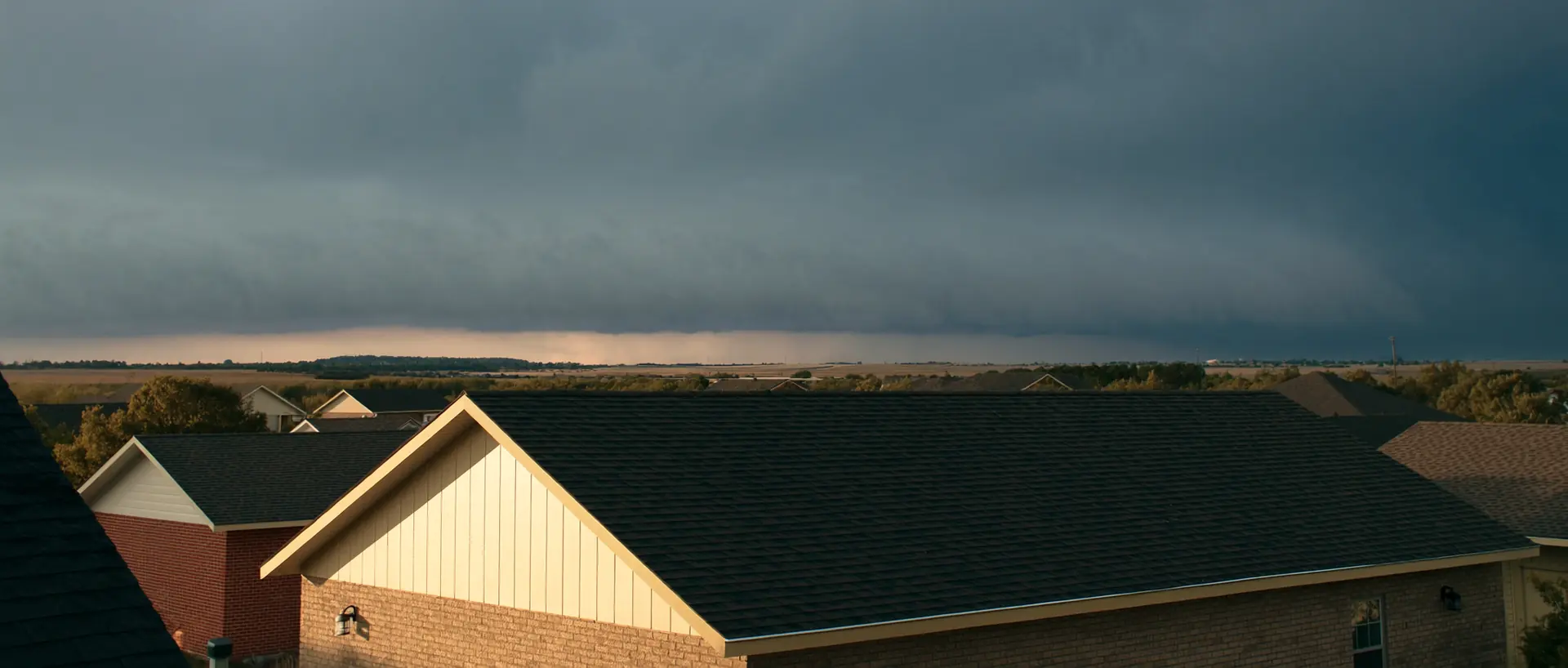 A storm shelf cloud building over suburban rooftops and open prairie in the Oklahoma City metro